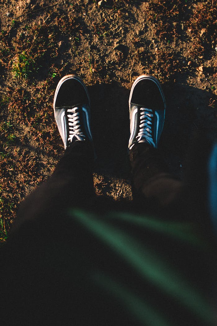 A top-down view of a person standing on a dirt path wearing casual sneakers, captured in warm natural light.